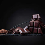 A pile of dark chocolate bars with cocoa powder on a black surface