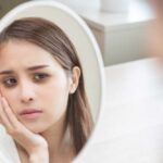 A young woman looking thoughtfully at her reflection in a mirror