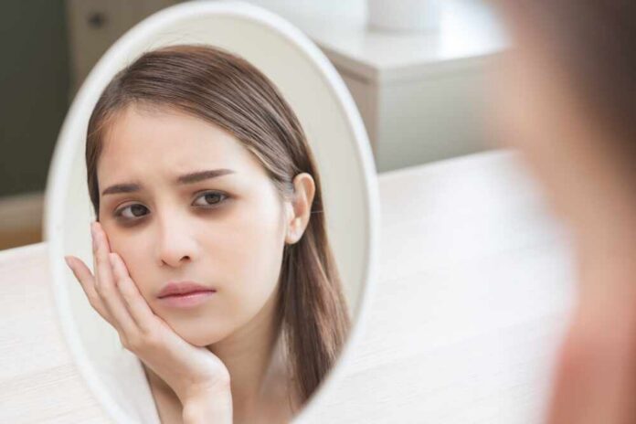 A young woman looking thoughtfully at her reflection in a mirror