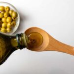 Olive Oil EXPOSÉ: Misleading Labels Unveiled Pouring olive oil from a bottle into a wooden spoon