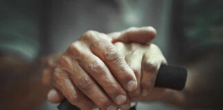 Close-up of elderly hands resting on a walking cane