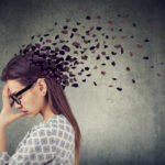 Stress-Induced Confusion: A Silent Epidemic? A woman with glasses holding her head, with fragments dispersing from her head