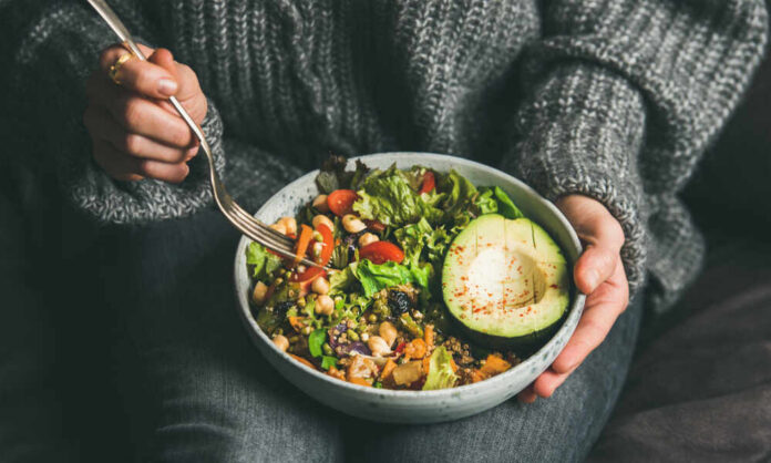 shutterstock_1317602774.jpg A person holding a bowl of colorful salad with avocado and greens