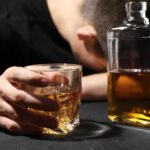 10-Minute Trick Slashes Depression by 20% A person with their head down, holding a glass of whiskey next to a bottle