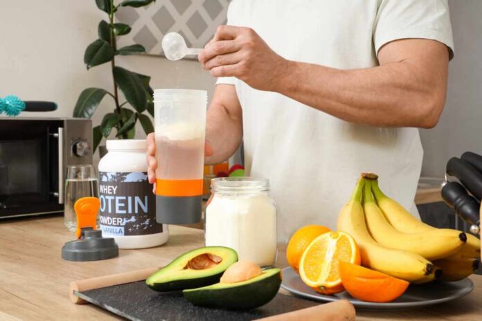 Person preparing a protein shake with fruits and whey protein powder in a kitchen