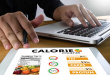 Person using a calorie counter app on a tablet while working on a laptop