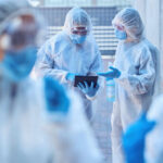 CDC’s Rapid Ebola ACTION: What’s At Stake? Healthcare workers in protective gear discussing information on a tablet outdoors