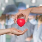 Two hands exchanging a red heart symbol in a surgical setting