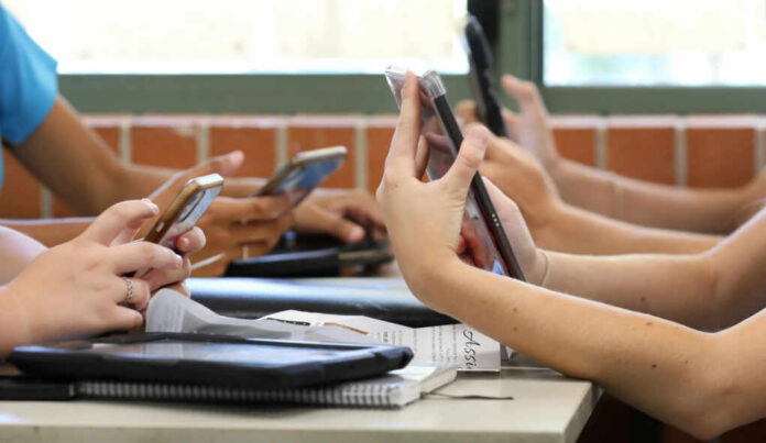 9a3727d6-ff70-4c52-bc15-2dd3fe515569_shutterstock_1847575498 Students in a classroom using smartphones for a group activity