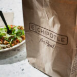 Takeaway Trap: Hidden Salt Overload A Chipotle takeout bag next to a bowl filled with fresh salad ingredients