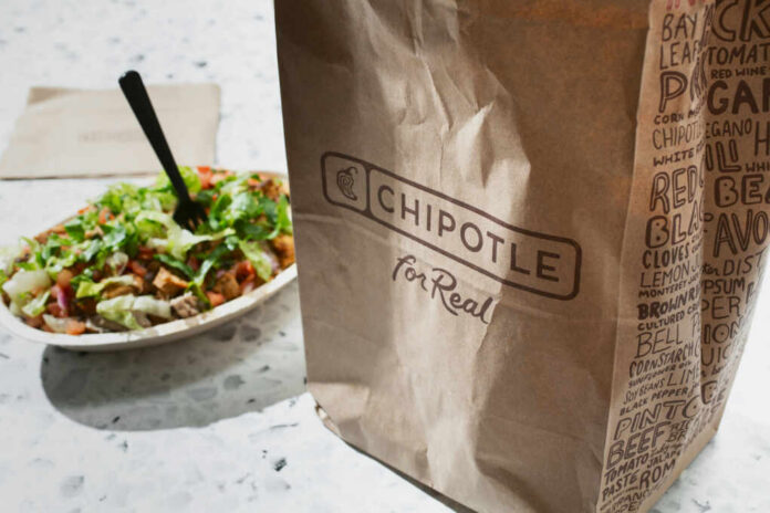 A Chipotle takeout bag next to a bowl filled with fresh salad ingredients