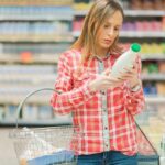Woman reading a bottle label in a grocery store aisle
