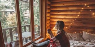 Woman wrapped in a blanket sitting on a bed by a cabin window