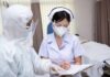 The New Norm for Respiratory Virus Prevention nurse in PPE writing on a clipboard with colleague