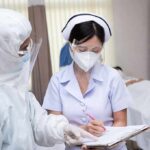 nurse in PPE writing on a clipboard with colleague