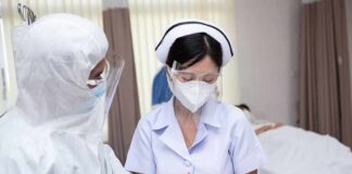 nurse in PPE writing on a clipboard with colleague