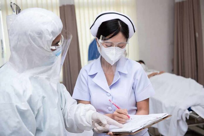 shutterstock_1823374517 nurse in PPE writing on a clipboard with colleague