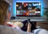 How long-term TV watching affects brain health in adults Person sitting on a couch watching a movie on a TV with popcorn in hand