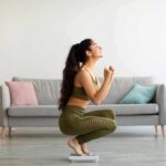 Woman in activewear kneeling on a bathroom scale