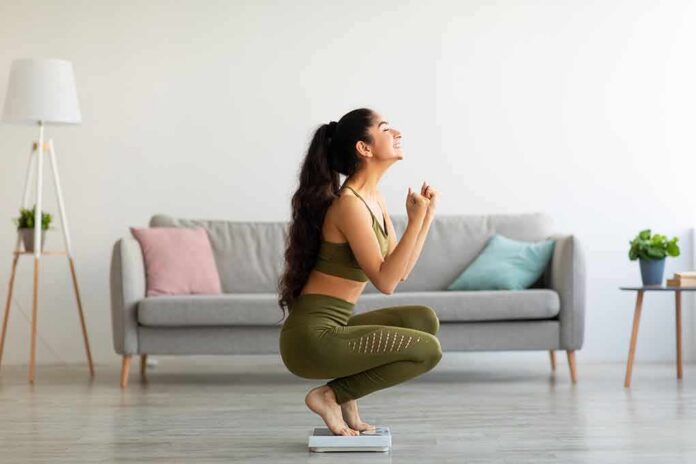Woman in activewear kneeling on a bathroom scale