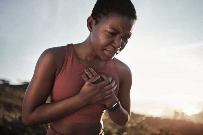 Black,Woman,,Runner,And,Heart,Attack,Pain,In,Nature,While A woman in athletic wear holding her chest with a pained expression outdoors