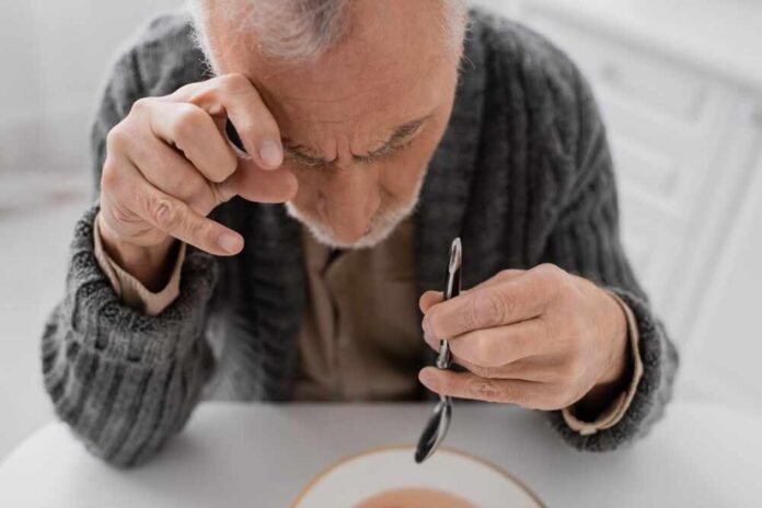 Senior,Man,Suffering,From,Parkinson,Disease,And,Hands,Tremor,Sitting Elderly man focusing intently on a spoon while preparing to eat