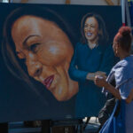 A woman admires a large portrait of a smiling female figure at an outdoor event