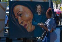 A woman admires a large portrait of a smiling female figure at an outdoor event