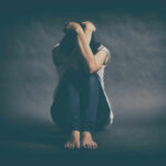 ‘Evil’ Or Mental Illness? Unraveling the Mystery A person sitting on the floor with their arms wrapped around their knees, conveying a sense of distress
