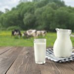 Milk jug and glass on wooden table with pasture in background