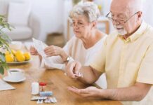 Older man taking pills at a table while woman reads instructions