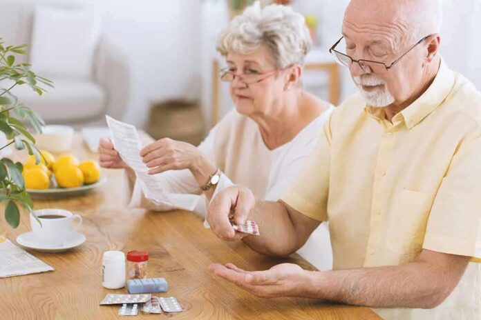 Older man taking pills at a table while woman reads instructions