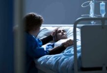 Patient in hospital bed with visitor holding their hand