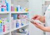 Pharmacist using a tablet in front of stocked pharmacy shelves
