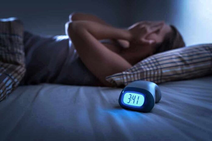 Person lying awake in bed beside a glowing digital alarm clock