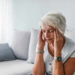 Everyday Habits That Increase Cortisol in Our Bodies Older woman sitting on a couch holding her temples
