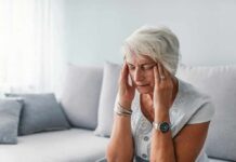 Older woman sitting on a couch holding her temples