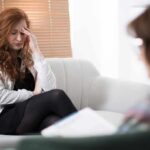 The Secret to Getting More Done Without Burning Out Woman with hand on forehead sitting on couch during therapy session
