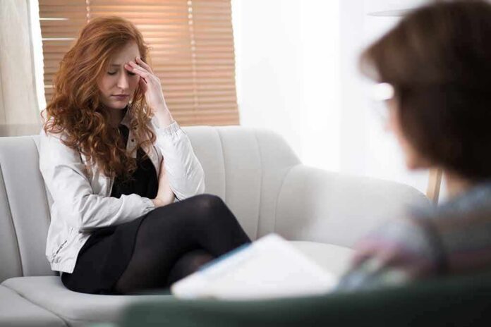 Woman with hand on forehead sitting on couch during therapy session