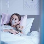 Genes That Decide Who Will Get Cancer Child in hospital bed with oxygen mask holding teddy bear