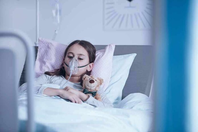 Child in hospital bed with oxygen mask holding teddy bear