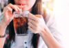 person sipping iced drink from a glass mug with a straw