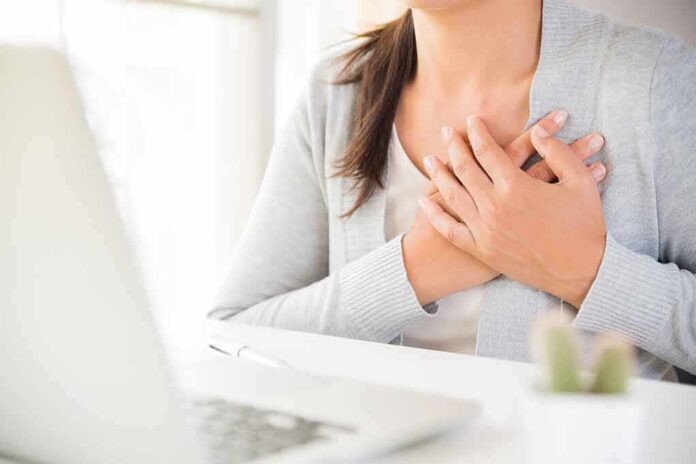 person clutching chest with both hands at a desk