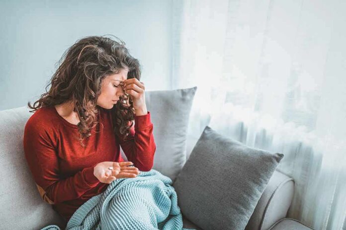 Woman sitting on couch holding pills and rubbing her forehead