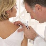 Hidden Psoriasis Twin That Turns Deadly Doctor examining a patients skin with a magnifying glass