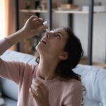 The One Deficiency Behind Dry Eyes and Dry Mouth Woman applying eye drops while seated on a couch