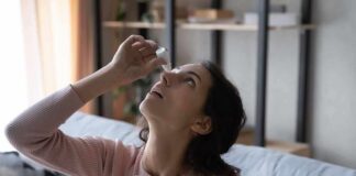 Woman applying eye drops while seated on a couch