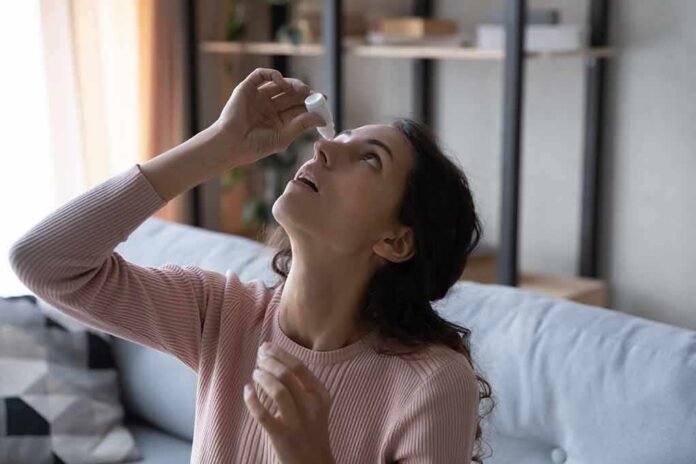 Woman applying eye drops while seated on a couch