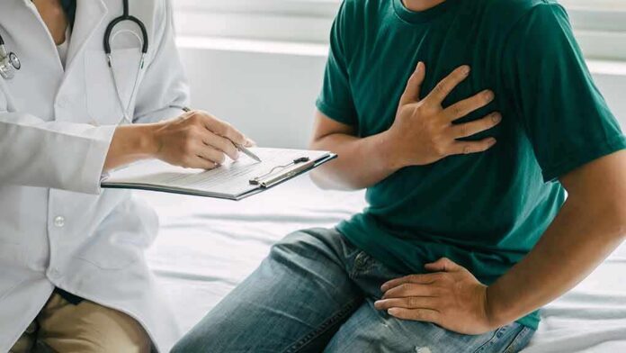 shutterstock_2275656477 Patient holding chest while doctor takes notes