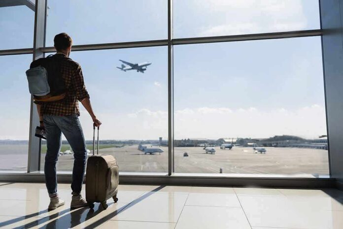Traveler with suitcase watching plane through airport window